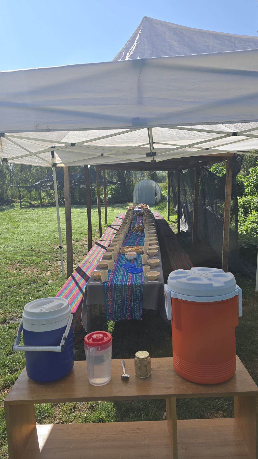Mesa de servicio bajo una carpa en la chinampa, con termos de bebidas